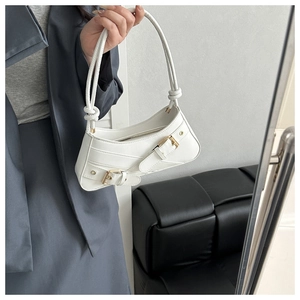 Close-up of white leather underarm bag featuring decorative straps and gold metal buckle