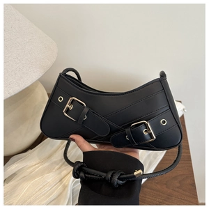 Detail of black crescent shoulder bag featuring double parallel gold buckles and knotted strap