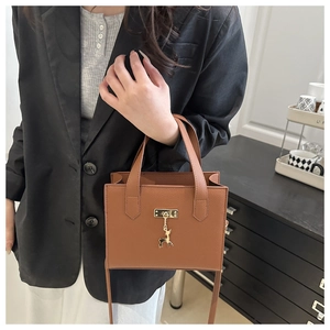 Détail du petit sac carré en cuir caramel avec texture litchi et pendentif cerf doré