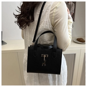 Détail d'un sac à main noir en cuir grainé avec finitions dorées et pendentif cerf