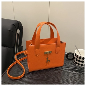 Détail du sac à main orange en cuir grainé avec finitions dorées et pendentif de cerf