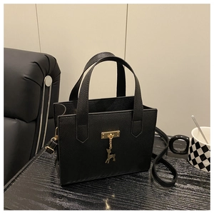 Détail du sac en cuir grainé noir avec boucle dorée et pendentif cerf sur un bureau