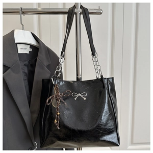 Detail of black glossy patent leather tote bag with silver chain and bow pendant