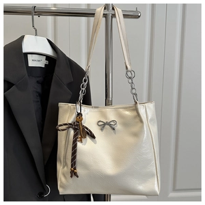 Detail of off-white tote bag with leather texture, silver bow, and metal chain straps