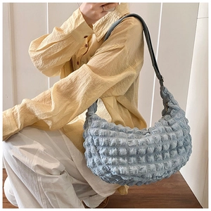 Detail of light blue bubble textured crescent shoulder bag with wide strap on model