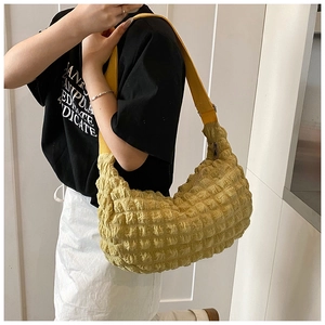 Detail of yellow pleated cloud bag showing bubbled texture and canvas shoulder strap on model