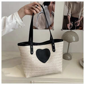 Détail d'un sac cabas tissé avec poignée en cuir noir et patch en cuir en forme de cœur