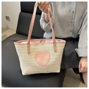 Détail d'un sac à main tissé en paille avec un patch coeur rose et des lanières assorties
