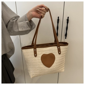 Détail du sac cabas en paille tressée avec écusson cœur en cuir marron et rivets en métal