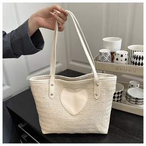 Détail du sac cabas beige tressé avec patch cœur en cuir et finitions de rivets