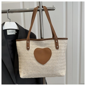 Détail d'un sac cabas en paille tressée avec écusson cœur en cuir et double anses