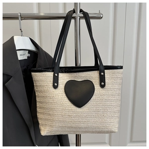 Détail d'un sac cabas tissé beige avec patch cœur en cuir noir et rivets métalliques