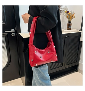 Detail of red shoulder bag featuring silver metal rivets on glossy synthetic leather