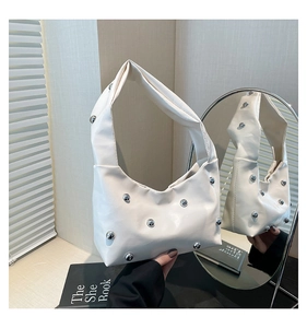 Close-up of white PU leather crescent bag featuring dense silver stud rivets and a sleek handle