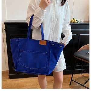 Blue canvas tote bag with contrast stitching and leather tag shown on shoulder