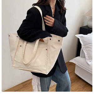 Gros plan du sac cabas en toile blanc cassé avec poche avant et rivets métalliques