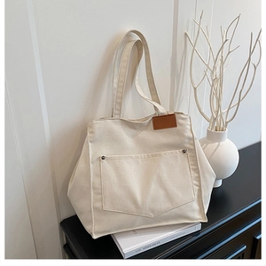 Detail of off-white canvas tote bag with metal rivet pocket and brown leather patch