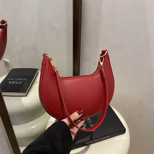 Minimalist red leather hobo bag with lychee texture and golden zipper held by hand