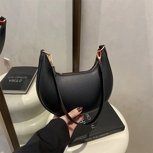 Black lychee leather crescent shoulder bag with gold hardware and vibrant red interior lining