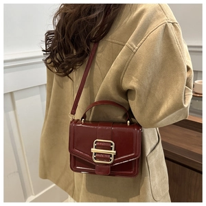 Detail of burgundy patent leather crossbody bag with gold buckle on a beige coat