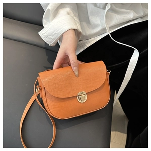 Macro shot of orange pebble leather crossbody bag featuring a round gold twist lock closure