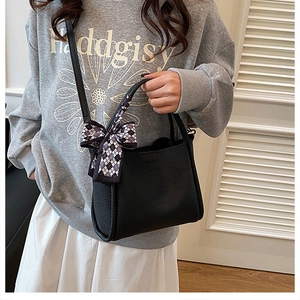 Detail of black pebbled leather bucket bag with a checkered bow tie and shoulder strap