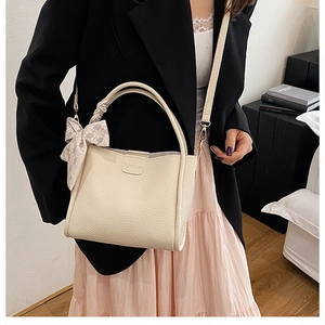 Detail of creamy white leather bucket bag with textured grain and elegant bow ribbon