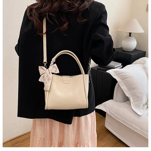Detail of beige bucket bag with lychee texture, silk scarf handle, and fashion logo
