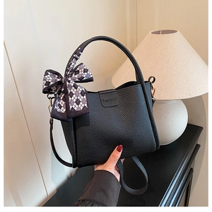 Close-up of black litchi grain bucket bag with silk scarf bow and fashion logo