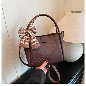 Detail of dark brown lychee texture leather bucket bag with plaid bow and fashion embossing