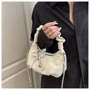 Detail of white pleated bag featuring pearl bow charm and glossy finish texture