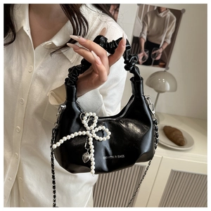 Detail of black cloud bag featuring a pearl bow charm and silver chain strap
