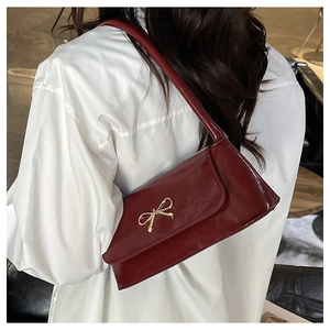 Gros plan d'un sac à bandoulière rouge foncé brillant avec boucle décorative en nœud doré