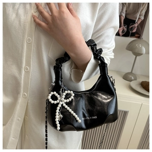 Close-up of black glossy pleated bag featuring pearl bow charm and metal chain strap