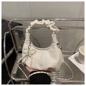 Detail of white glossy crescent bag with ruched handle, pearl bow, and silver chain strap
