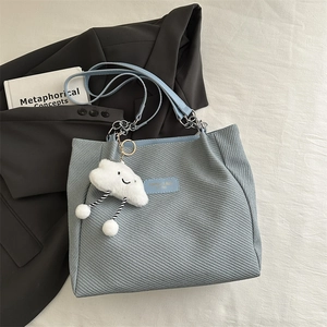Light blue twill tote bag with chain strap and cloud plush charm in casual flat lay