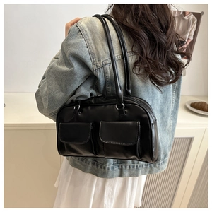Detail of glossy black shoulder bag with dual front pockets and silver metal buckles