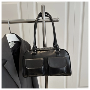 Detail view of black glossy shoulder bag with dual front pockets hanging on a rack