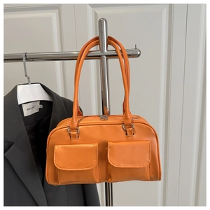 Detail view of glossy orange underarm bag with double front flap pockets and slim handles