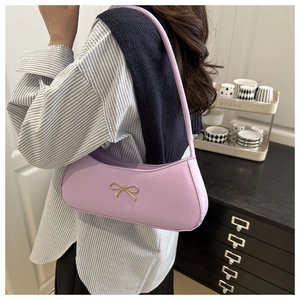 Detailed view of light purple leather bag featuring a gold metal bow and smooth texture