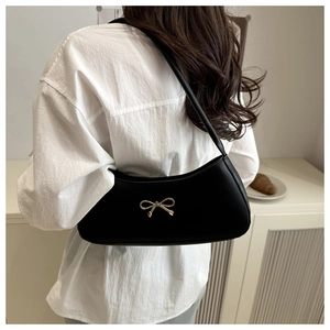 Close-up of a black leather underarm bag featuring a gold bow detail on a female model