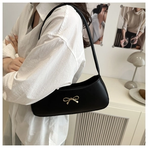 Detail shot of black faux leather underarm bag featuring a golden bow metal clasp decoration