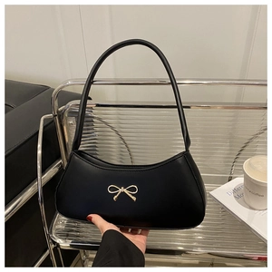 Close-up of black matte leather shoulder bag with gold metal bow and sleek crescent shape