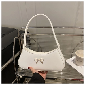 Close-up of a white crescent shoulder bag with a gold metal bow on a leather surface