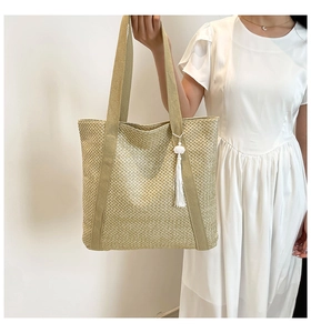 Détail du sac cabas en paille tissée avec anses en toile et pendentif pompon nuage blanc