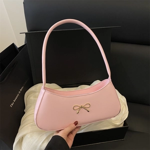 Pink underarm baguette bag with a gold metal bow on black gift box and white silk
