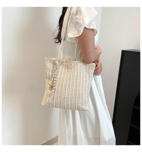 Detail of straw woven tote bag with striped ribbon and gold spherical charm accent