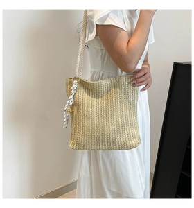 Detail of beige woven straw tote bag with black and white striped ribbon and gold bell