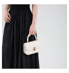 Detail of a minimalist cream white handbag with golden lock and smooth PU leather texture