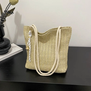 Handmade straw tote bag with rope handles and decorative bell on black wooden surface